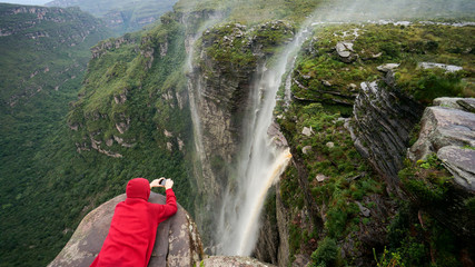 Traveler lies on the edge of the cliff and taking a picture of the waterfall in Chapada Diamantina national park, State of Bahia, Brazil.