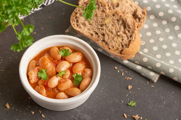 Baked beans in tomato sauce on black stoneware with bread, meal.