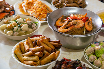 Casseroled prawns with Glass Noodels in Small Iron Pan with Fish, Fried Spring Rolls, Dim Sum, Seafood, Roasted Duck and Meatball Background on the Table.