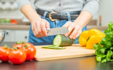 Fotobehang Woman is cutting cucumber on cut board on kitchen. © Dmytro Flisak