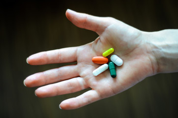Open female thenar holding two white, red, green, yellow pills, on a dark background