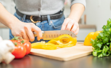 Woman is cutting yellow pepper on cut board on kitchen.
