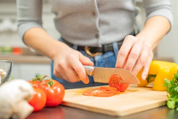 Fotobehang Woman is cutting tomatoes on cut board on kitchen. © Dmytro Flisak