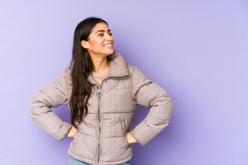 Young indian woman isolated on purple background laughs happily and has fun keeping hands on...