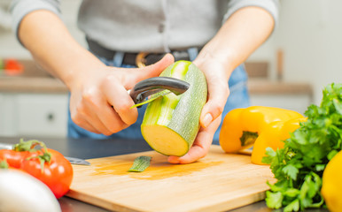 Woman peeling off zucchini on kitchen