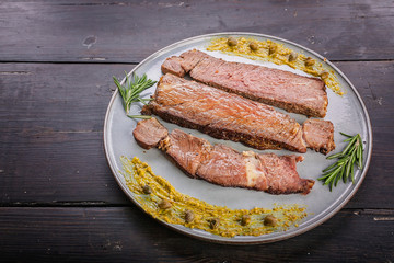 Close-up beef steaks with spices and sauce on a round gray plate on a dark wooden background.
