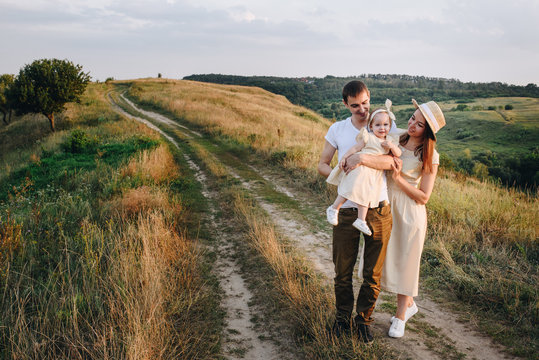 Family, mom, dad, daughter are walking on a hill in the field. Mom and daughter in yellow identical dresses.