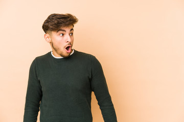 Young arabian man isolated on a beige background being shocked because of something she has seen.