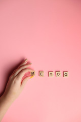 Woman hand making MeToo word with wooden alphabet on pink background, used for concept of sexual harrassment.