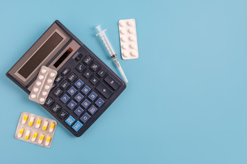 Calculator, syringe and medicine pills on blue background. cost of health care concept