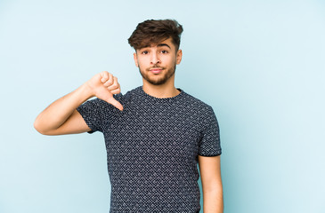 Young arabian man isolated on a blue background showing a dislike gesture, thumbs down....