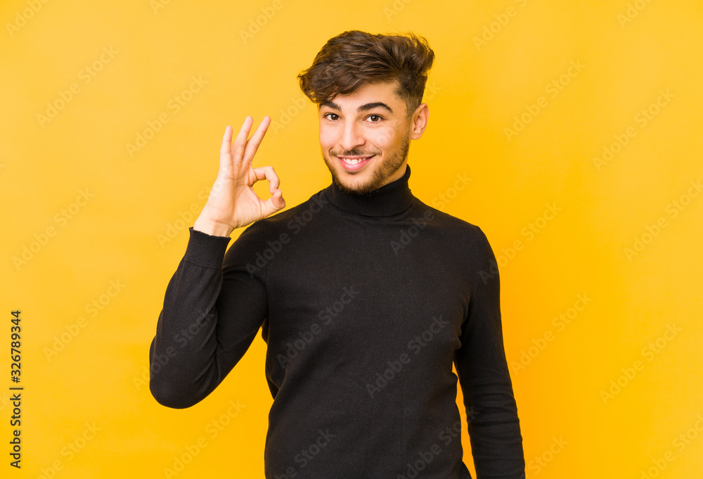 Wall mural young arabian man isolated on a yellow background cheerful and confident showing ok gesture.