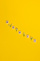 Top view word women spelled in wooden blocks on yellow background with flowers between them. Love,...