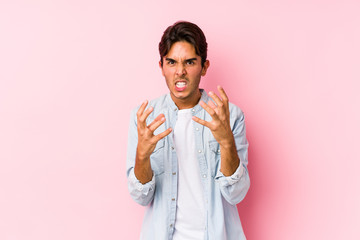 Young caucasian man posing in a pink background isolated upset screaming with tense hands.