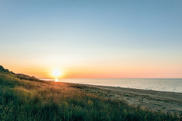 Green hill and sandy beach at sunset. Evening sea landscape with low sun on horizon..Peresyp resort village, Krasnodar region, Russia.