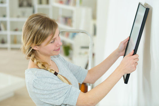 woman hanging art picture on wall