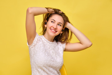 Fototapeta premium A girl in summer clothes stands on a yellow background and listens to music in wireless headphones while enjoying her and pulls her hair.