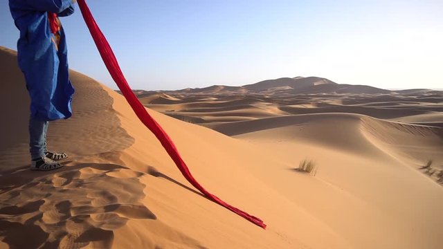 Local berber man puts red headscarf on his head on the sand desert in the middle of hot day in Morocco 
