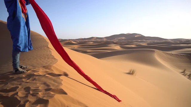 Local berber man puts red headscarf on his head on the sand desert in the middle of hot day in Morocco 