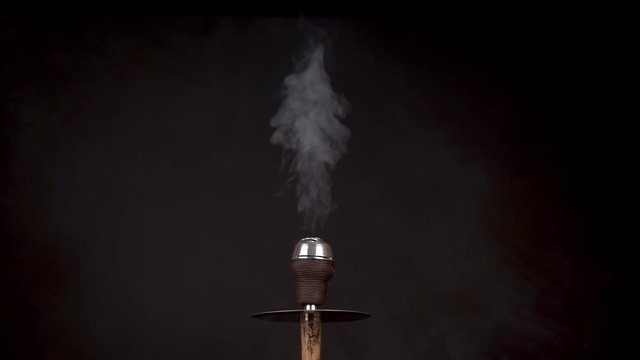 White smoke evaporates upwards from a beautiful beige hookah while purging against a black background close up. The concept of cleaning the bitter taste of burnt tobacco. Slow motion.