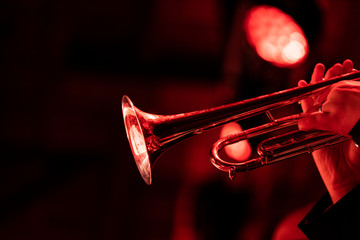 A trumpet player playing the trumpet in a big band concert on stage with red stage lights with bokeh in the background