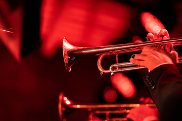 Fototapeta premium Two trumpet players playing their instrument in the trumpet section of a big band during a concert with red stage lights