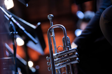 A silver plated trumpet resting on a stand with a stand light in the back during a big band concert