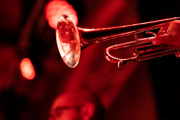 A trumpet player playing the trumpet in a big band concert on stage with red stage lights with...