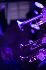  The trumpet section of a big band is playing a chorus during a concert on stage in purple stage lights