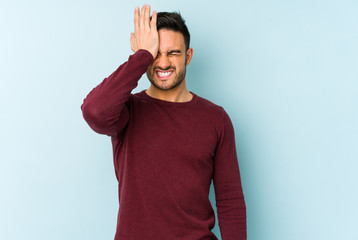 Young caucasian man isolated on blue background forgetting something, slapping forehead with palm...