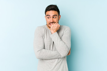 Young caucasian man isolated on blue background biting fingernails, nervous and very anxious.