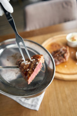 The waiter is holding a plate Grilled striploin steak with Pickled cabbage and two sauces. The strip steak, also called a New York strip. Serving on a wooden Board. Barbecue restaurant menu.