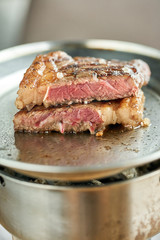 Metal Plate on red coal with Grilled striploin steak . The strip steak or New York strip. Barbecue restaurant menu. Medium rare