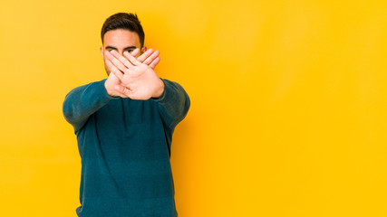 Young caucasian man isolated on yellow bakground doing a denial gesture