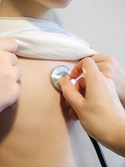 Fototapeta premium Doctor's hand with stethoscope listens to breathing of child in white T-shirt. Health care, treatment of cold and respiratory viral diseases concept.