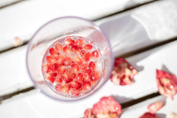 glass with water and pomegranate berries on a blurred background