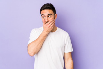 Young caucasian man isolated on purple background thoughtful looking to a copy space covering mouth with hand.