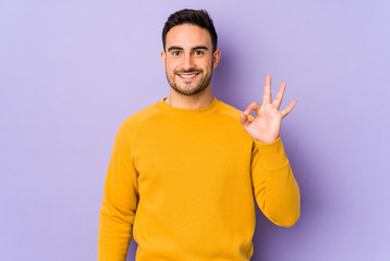 Young caucasian man isolated on purple background cheerful and confident showing ok gesture.