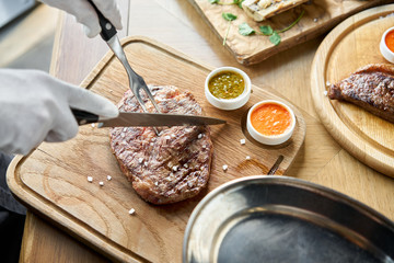 The waiter cutting Rib eye steak on wooden board. Barbecue restaurant menu.