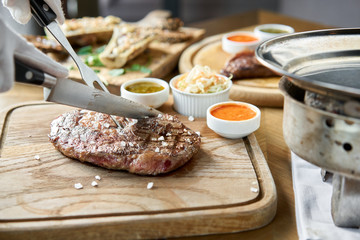 The waiter cutting Rib eye steak on wooden board. Barbecue restaurant menu.