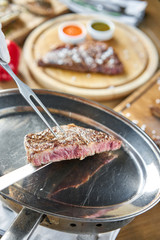 The waiter is holding a plate Grilled striploin steak with Pickled cabbage and two sauces. The strip steak, also called a New York strip. Serving on a wooden Board. Barbecue restaurant menu.