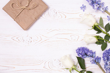 A gift box wrapped in craft paper and blue hyacinth flowers, white roses on a white table top. Flat lay. Copy space for text