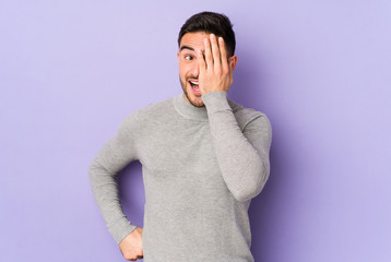 Young caucasian man isolated on purple background having fun covering half of face with palm.