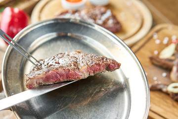The waiter is holding a plate Grilled striploin steak with Pickled cabbage and two sauces. The strip steak, also called a New York strip. Serving on a wooden Board. Barbecue restaurant menu.