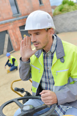 man on industrial vehicle shouting to colleague