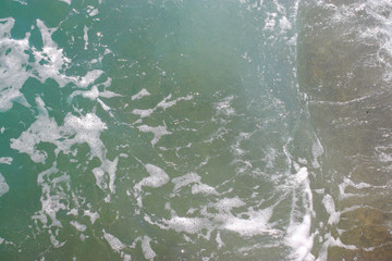 Top view texture waves, foaming and splashing in the ocean, sunny day.  Beautiful tropical sea in summer season image by aerial view. Abstract sea background. Ocean waves close-up.