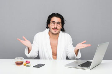 Young handsome man working after a shower doubting and shrugging shoulders in questioning gesture.