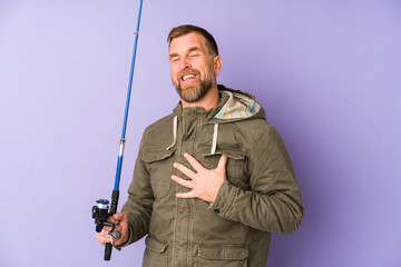 Senior fisherman isolated on purple background laughs out loudly keeping hand on chest.