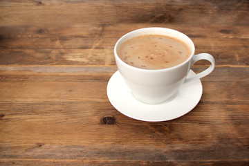 cappuccino coffee in a white cup and saucer with copy space on an old wooden table, concept of a stylish cafe