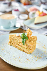 Honey sponge cake decorated with meringue and mint leaves.. Breakfast in the cafe, morning coffee. Cappuccino and lots of desserts on the table.